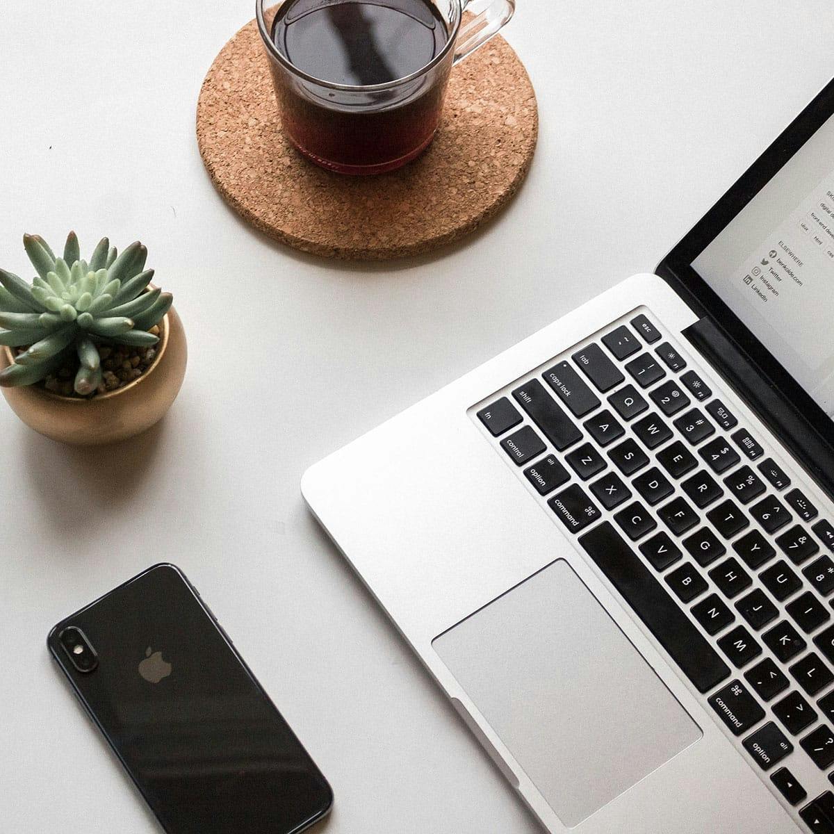Skrivebord med laptop, kaffe og en liten plante